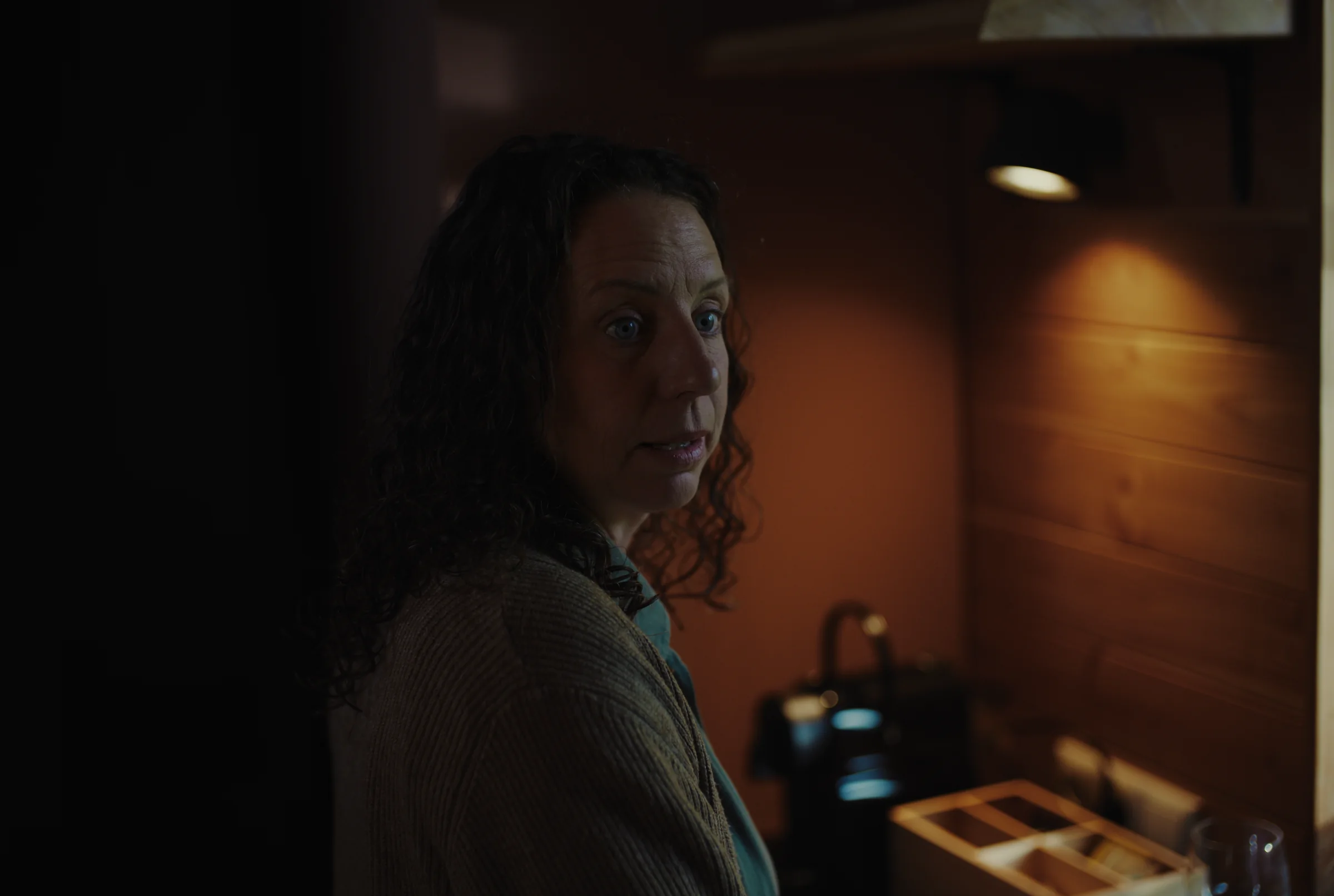 A woman looks back in a dimly lit room.