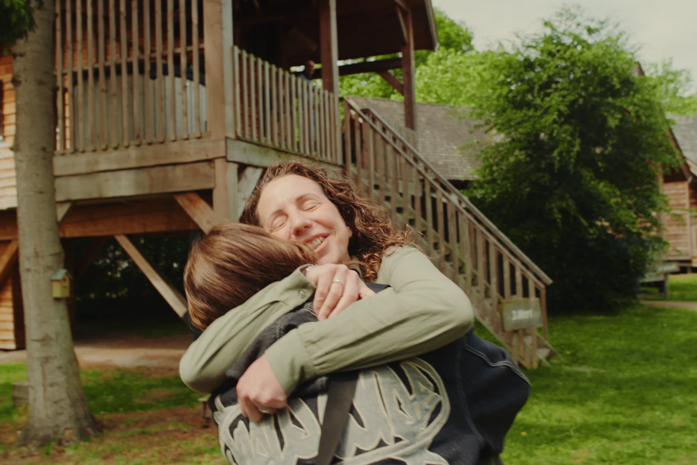 A woman and child embrace outside a house.