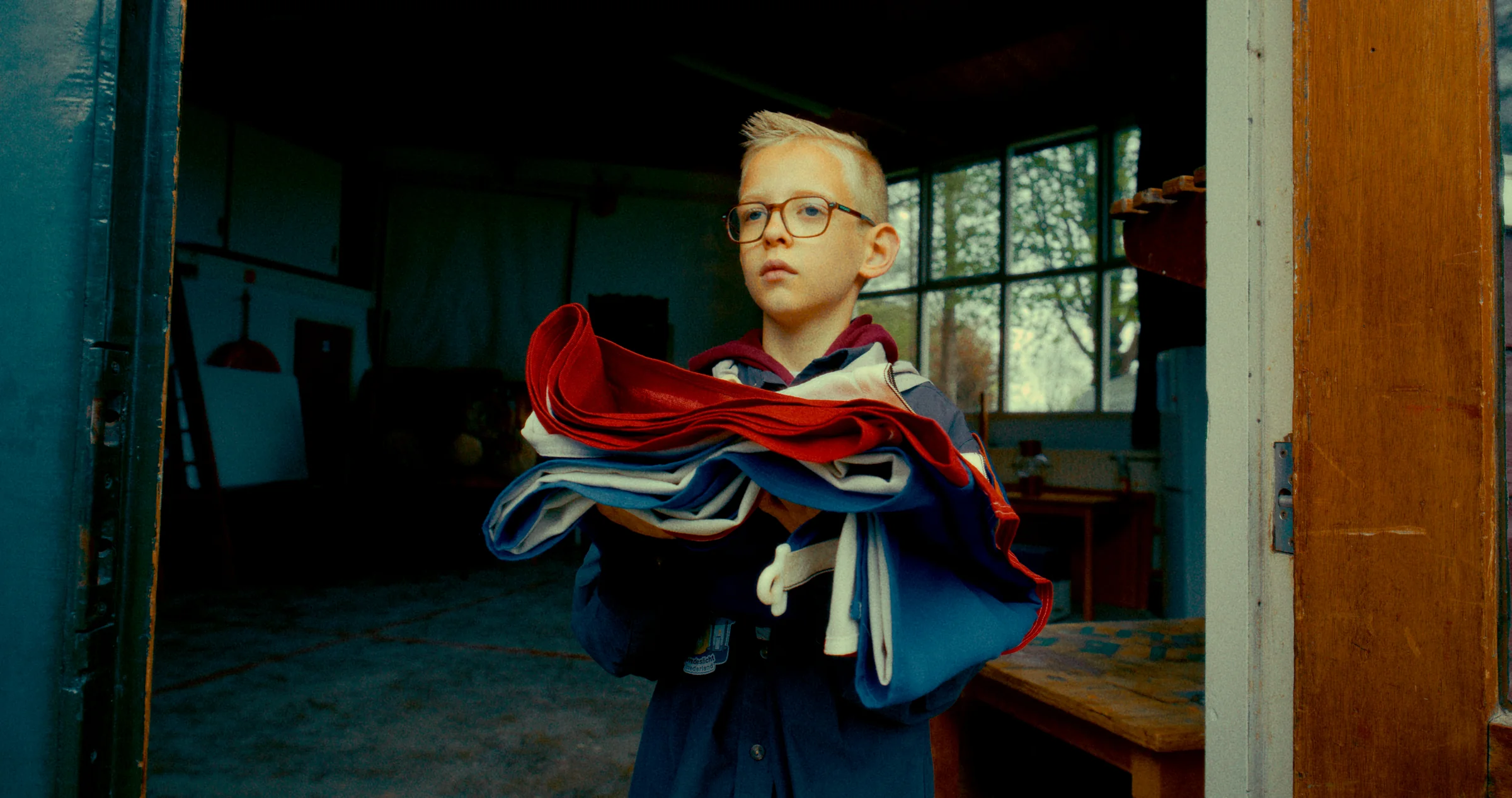 A young man holds a stack of clothes in a doorway.
