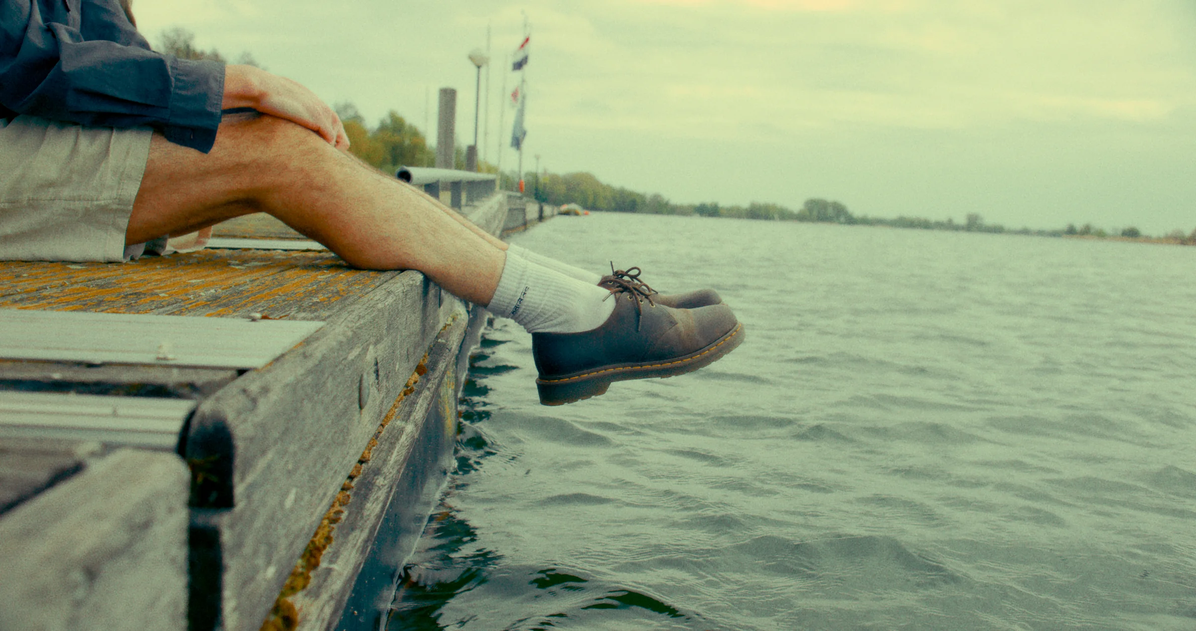 A person sits on a wooden dock above the water.