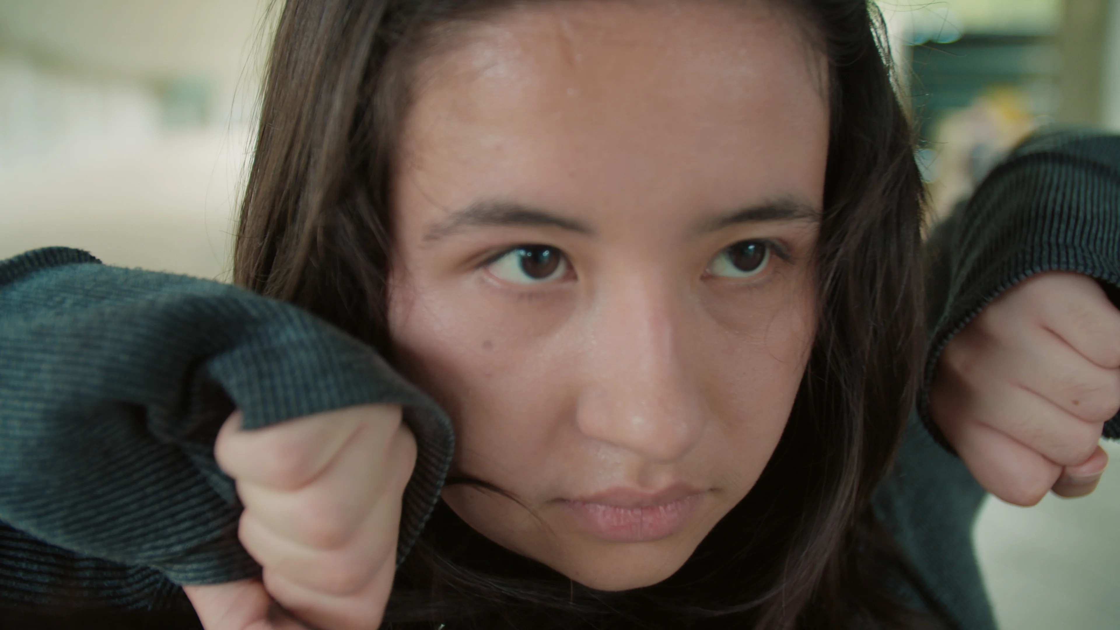 A young woman looks ahead from beneath her sleeve.