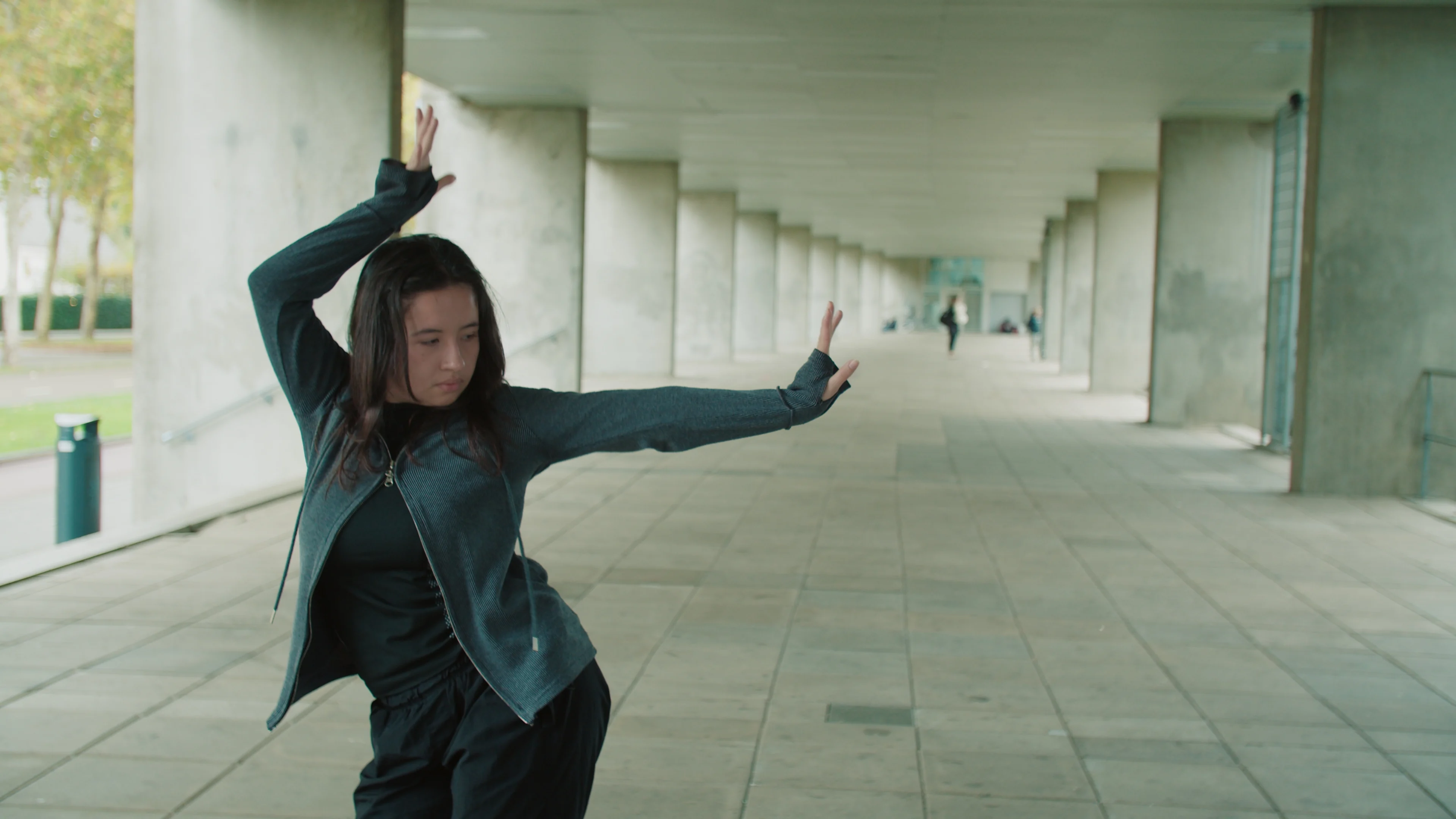 A dancer stretches her arms in a concrete corridor.