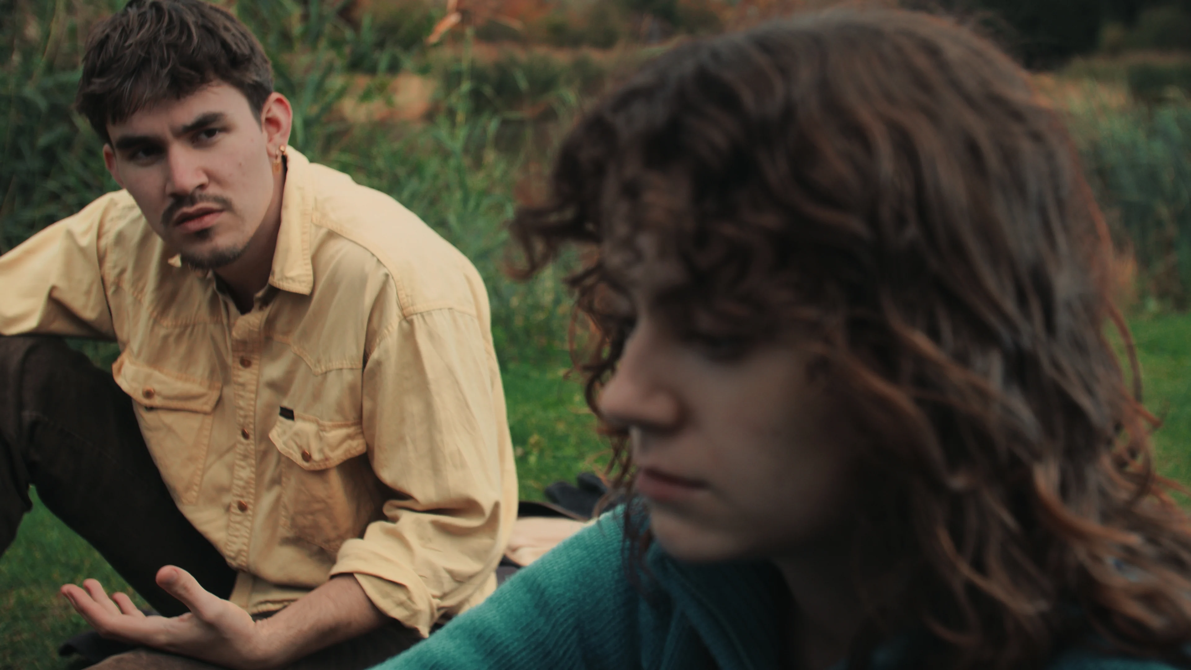 Two people sit together in a grassy field.