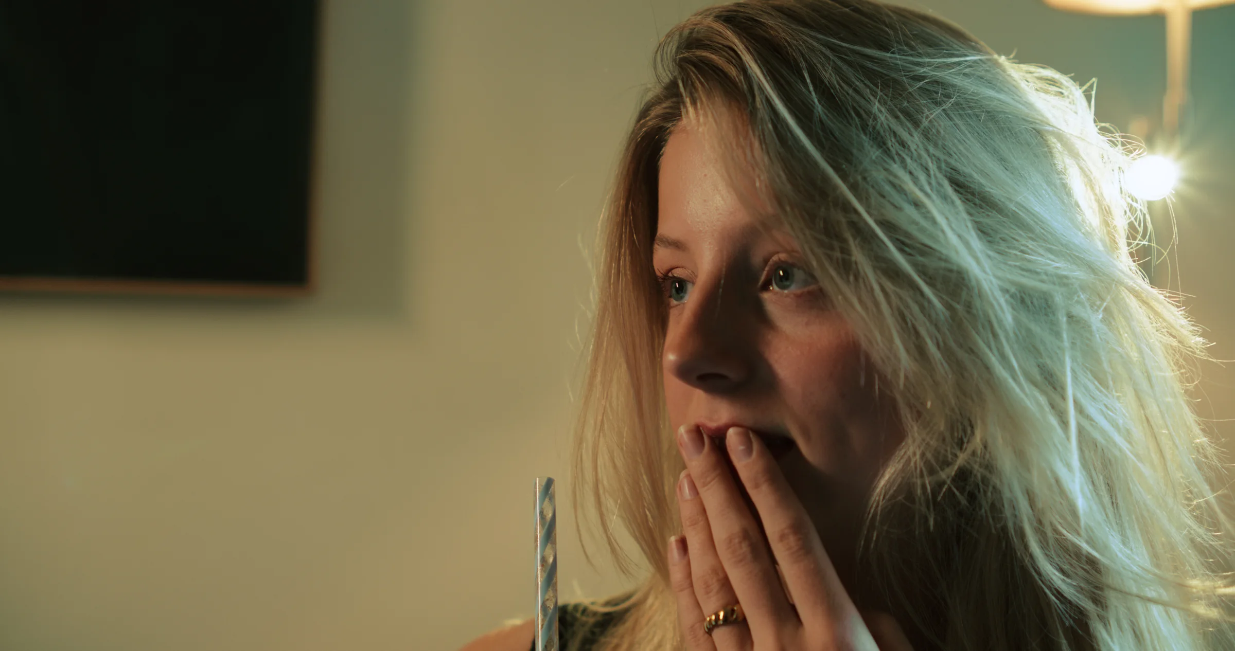 A woman sits in warm light with her hands near her face.