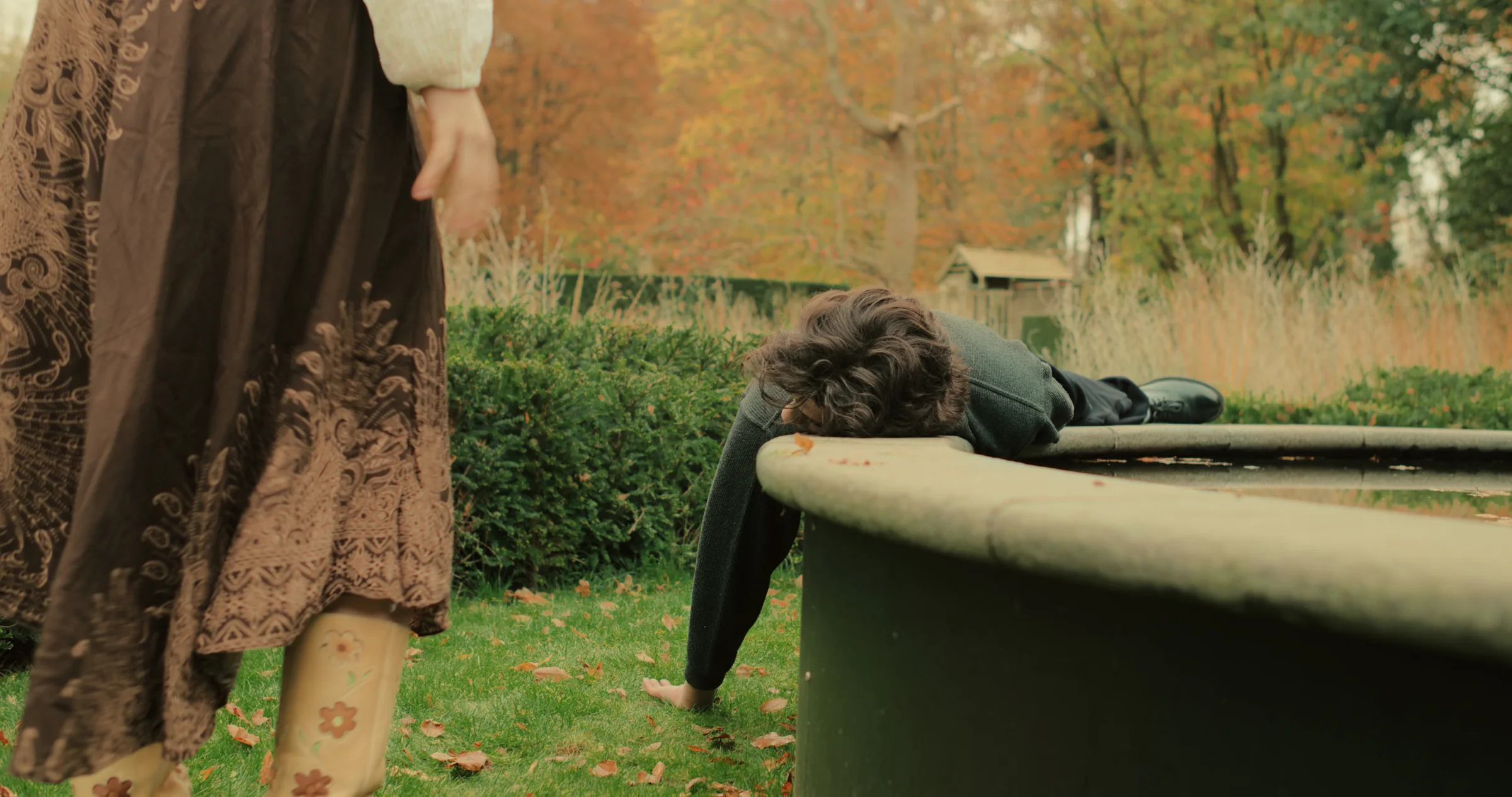 A figure leans over a low tub outdoors.
