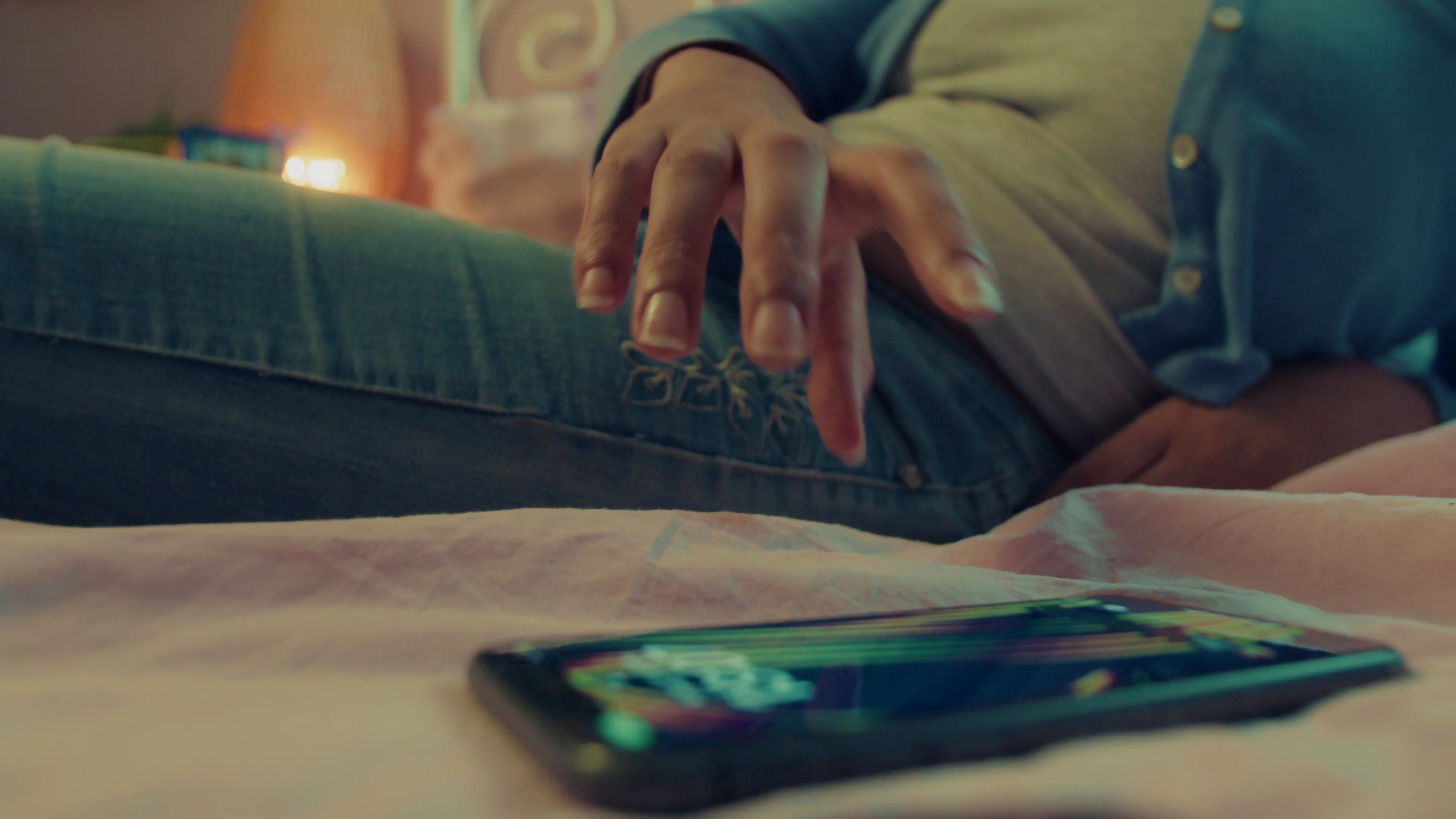 A quiet gesture above a phone resting on a bed.